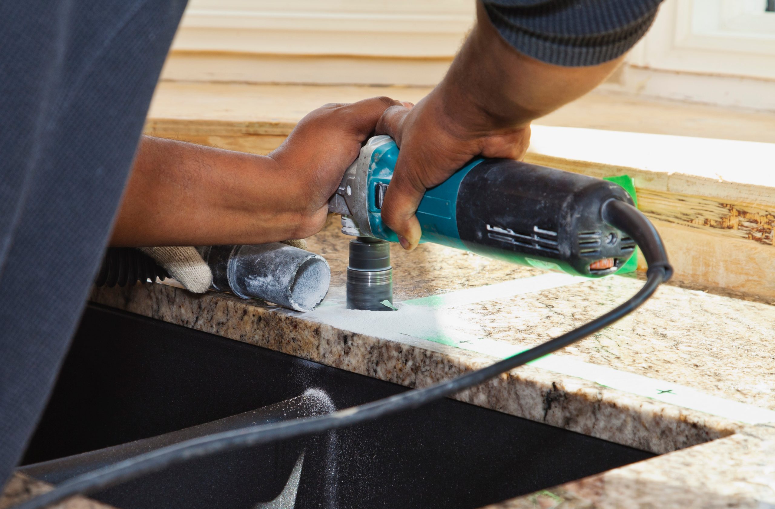 A worker installing a kitchen faucet into a newly set granite countertop during a countertop installation.